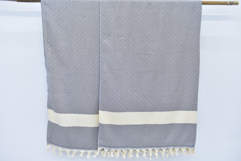 May include: Two gray towels with white stripes and fringe. The towels are hanging on a wooden rod.