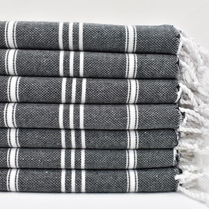 May include: A stack of black and white striped towels with white fringe. The towels are folded neatly and are ready to be used.