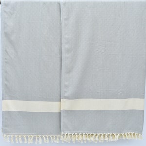 May include: Two gray and white striped towels with fringe on the bottom. The towels are hanging from a wooden rod.