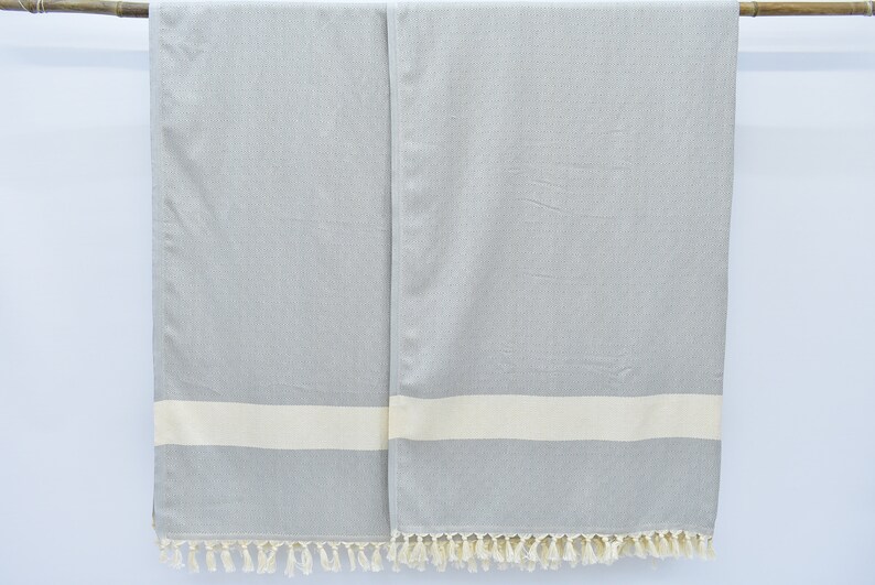 May include: Two gray and white striped towels with fringe on the bottom. The towels are hanging from a wooden rod.