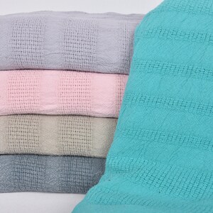 May include: A stack of four waffle weave blankets in different colors. The top blanket is light purple, the second is pink, the third is beige, and the bottom is light blue.