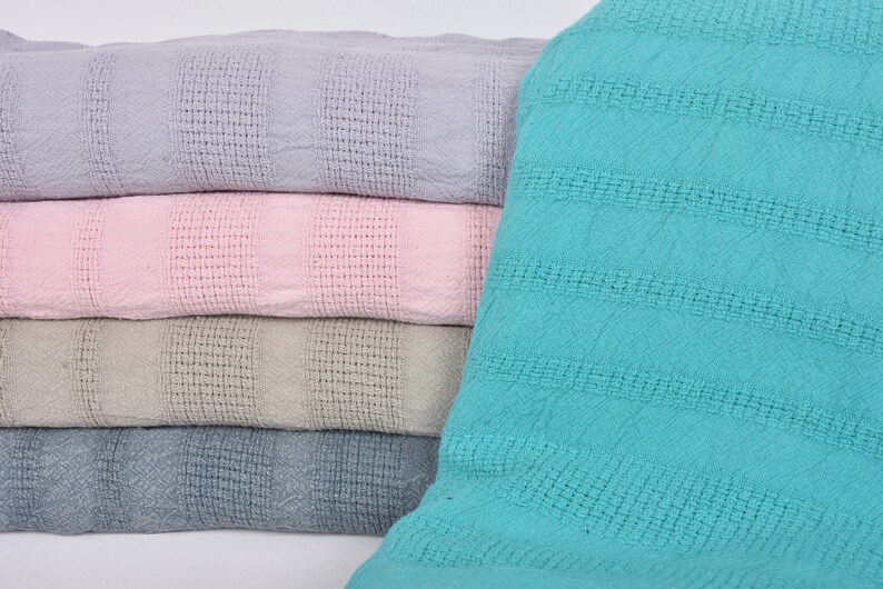 May include: A stack of four waffle weave blankets in different colors. The top blanket is light purple, the second is pink, the third is beige, and the bottom is light blue.