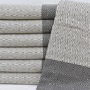 May include: A stack of white Turkish towels with black geometric patterns. The towels have a woven texture and are folded neatly.