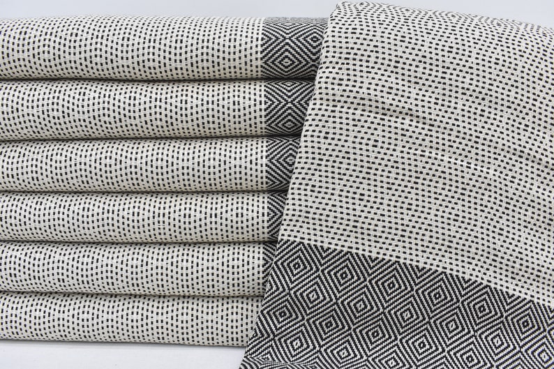 May include: A stack of white Turkish towels with black geometric patterns. The towels have a woven texture and are folded neatly.