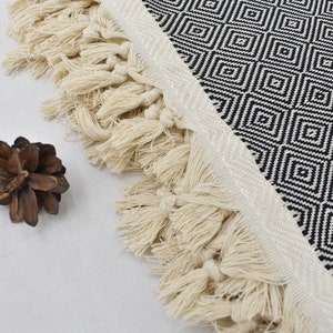 May include: Black and white geometric patterned throw blanket with a fringe border. The fringe is made of natural fibres and is a light cream colour.