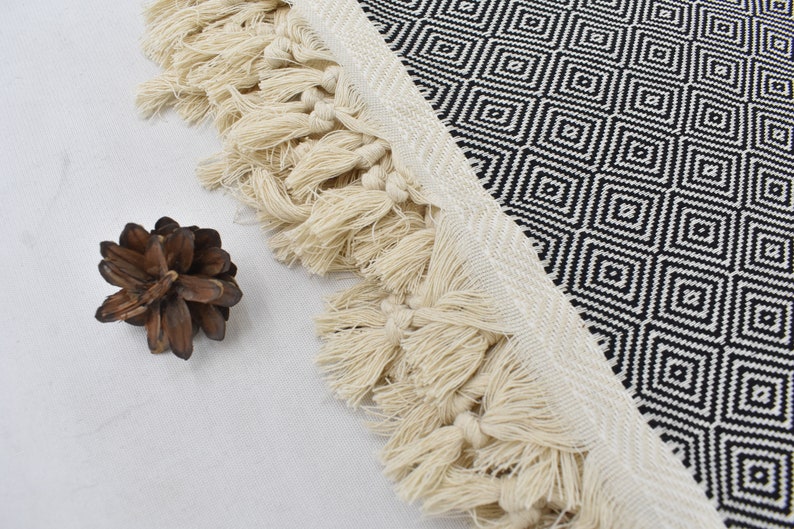 May include: Black and white geometric patterned throw blanket with a fringe border. The fringe is made of natural fibres and is a light cream colour.