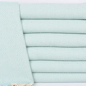 May include: A stack of light blue Turkish towels with a white diamond pattern and white fringe.