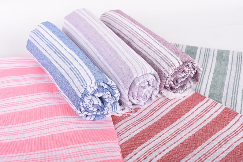 Puede incluir: Toallas a rayas enrolladas en tonos rosa, azul, morado, rojo y verde. Las toallas tienen rayas blancas y un borde con flecos. Las toallas est&aacute;n hechas de un material suave y absorbente, ideal para el ba&ntilde;o o la playa.