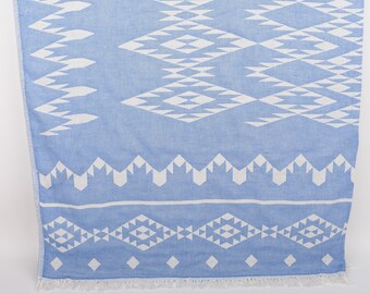 May include: A light blue and white patterned beach towel. The towel features a geometric design with diamond and zigzag shapes. The bottom edge has a fringe.
