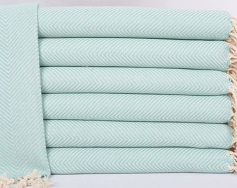 May include: A stack of six folded, light turquoise and white herringbone-patterned towels. The towels have a fringed edge on one side. The towels are made of a soft, absorbent material, perfect for use in a bathroom or at the beach.