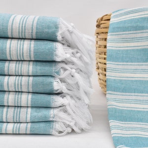 May include: A stack of blue and white striped towels with white fringe. The towels are folded and stacked on a white surface.