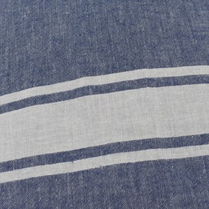 Op de afbeelding: Een blauwe en witte gestreepte stof met een textuurweefsel. De stof heeft twee witte strepen op een blauwe achtergrond.