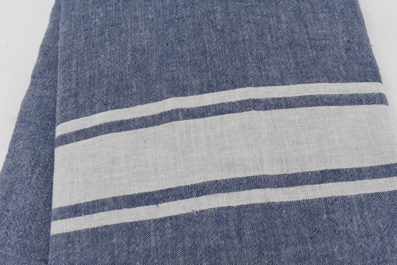 Op de afbeelding: Een blauwe en witte gestreepte stof met een textuurweefsel. De stof heeft twee witte strepen op een blauwe achtergrond.