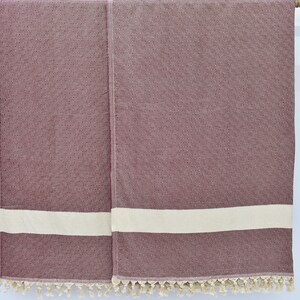 May include: Two burgundy towels with white stripes and tassels hanging on a wooden rod.