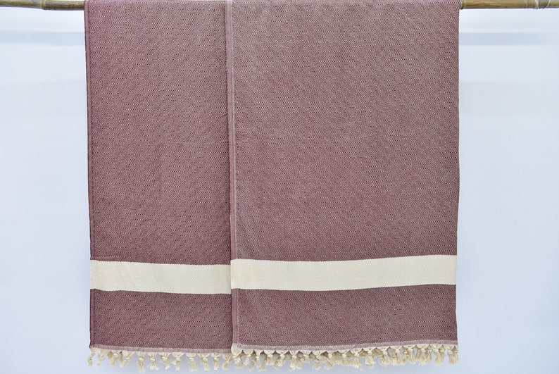 May include: Two burgundy towels with white stripes and tassels hanging on a wooden rod.