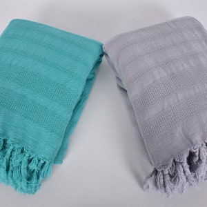 May include: Two folded Turkish towels, one teal and one light gray, with fringe on the edges.