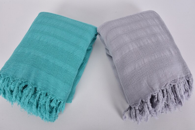 May include: Two folded Turkish towels, one teal and one light gray, with fringe on the edges.