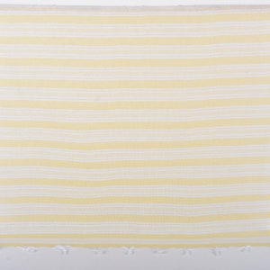 Puede incluir: Una toalla de playa a rayas amarillas y blancas colgada de una vara de madera. La toalla tiene rayas horizontales y un borde con flecos. La combinaci&oacute;n de colores es amarillo brillante y blanco.