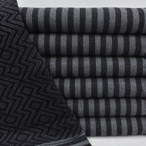 May include: A stack of black and gray striped towels with a black and gray geometric patterned towel on the left side. The towels have fringe on the ends.