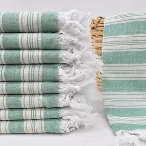 May include: A stack of green and white striped towels with white fringe. The towels are folded and stacked on a white surface.
