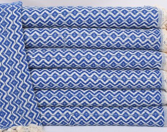 May include: A stack of blue and white patterned Turkish towels with fringe. The towels are folded and stacked on a white surface.