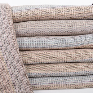 Könnte beinhalten: Ein Stapel von sechs gemusterten Wolldecken mit Fransen an den Rändern. Die Decken sind in den Farben Beige, Braun, Blau und Weiß gehalten.