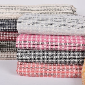 May include: A stack of woven fabric in various colors and patterns, including beige, black, pink, red, and orange. The fabric has a textured, waffle-like weave.
