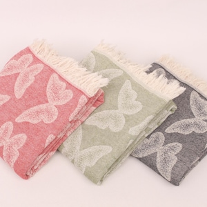 May include: Three folded decorative towels with a butterfly pattern. The towels are in shades of pink, green, and gray, with white butterfly designs. Each towel has a fringed edge.