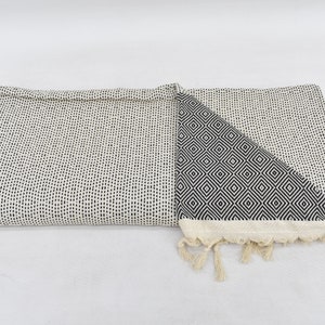 May include: A white and black patterned throw blanket with fringe. One side of the blanket features a small, black, geometric pattern. The other side features a larger, black, geometric pattern.