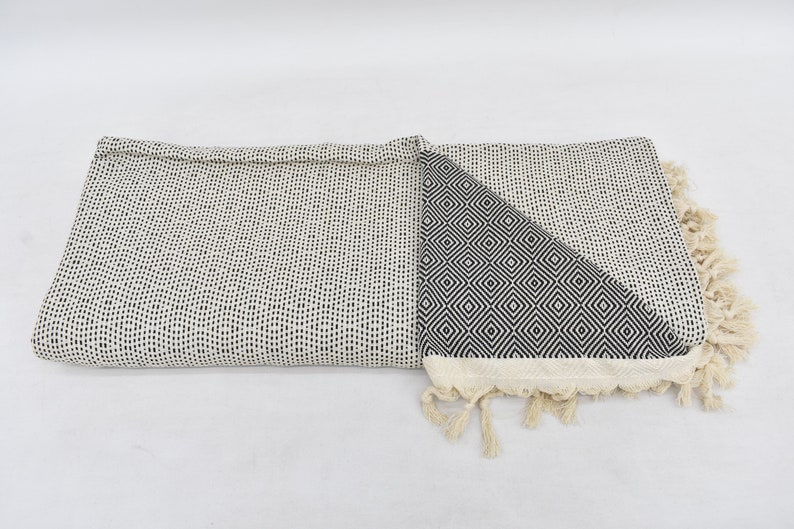 May include: A white and black patterned throw blanket with fringe. One side of the blanket features a small, black, geometric pattern. The other side features a larger, black, geometric pattern.