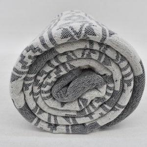 K&ouml;nnte beinhalten: Ein zusammengerolltes wei&szlig;es und graues t&uuml;rkisches Handtuch mit Muster. Das Handtuch ist aus Baumwolle und hat einen Fransenrand.