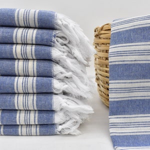 May include: A stack of blue and white striped towels with white fringe. The towels are folded and stacked on a white surface.