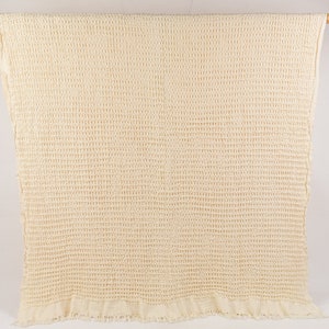 May include: A cream-colored waffle weave throw blanket with a fringed edge.