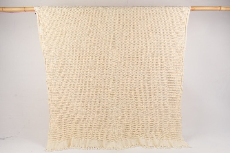 May include: A cream-colored waffle weave throw blanket with a fringed edge.