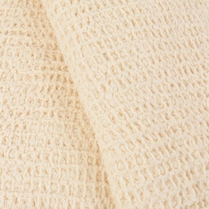May include: Close-up of a cream-colored waffle weave fabric. The fabric has a textured, waffle-like pattern.