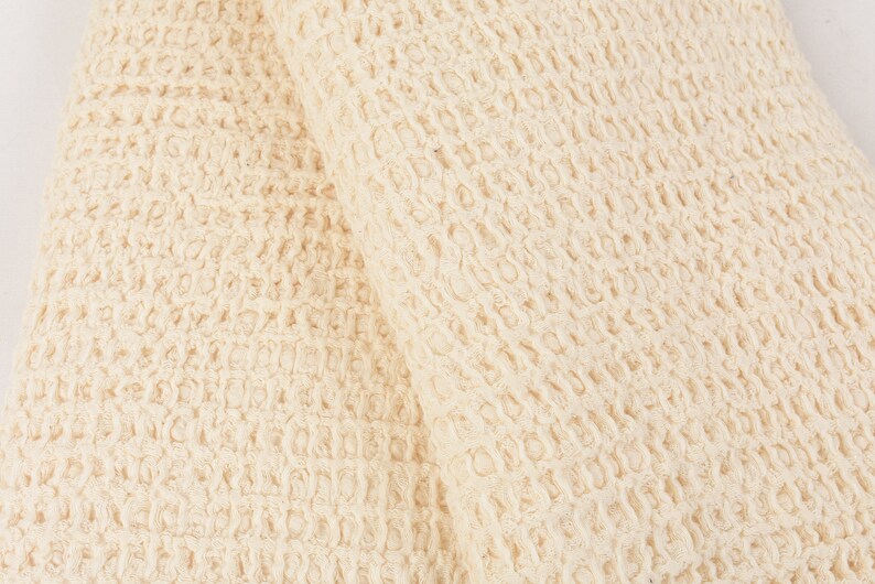 May include: Close-up of a cream-colored waffle weave fabric. The fabric has a textured, waffle-like pattern.