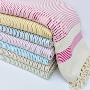 May include: A stack of colorful striped towels with fringed edges. The towels are folded and arranged in a rainbow pattern, with the top towel being pink and white.