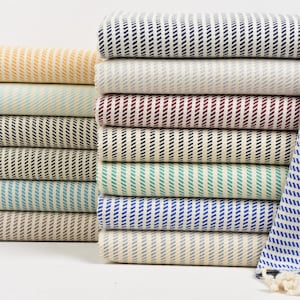 Op de afbeelding: Een stapel gestreepte handdoeken in verschillende kleuren, waaronder geel, blauw, groen, rood en zwart. De handdoeken zijn gevouwen en gestapeld op een wit oppervlak.