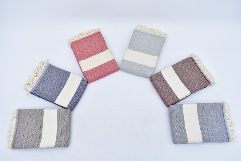 May include: Six Turkish towels in different colors, including gray, blue, red, and brown. Each towel has a white stripe in the center and fringe around the edges.