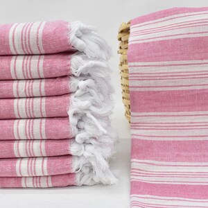 May include: A stack of pink and white striped towels with white fringe. The towels are folded and stacked on a white surface.