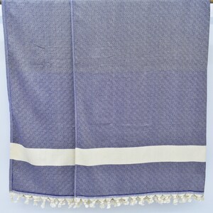 May include: A blue and white striped towel with fringe trim. The towel is hanging on a wooden rod.