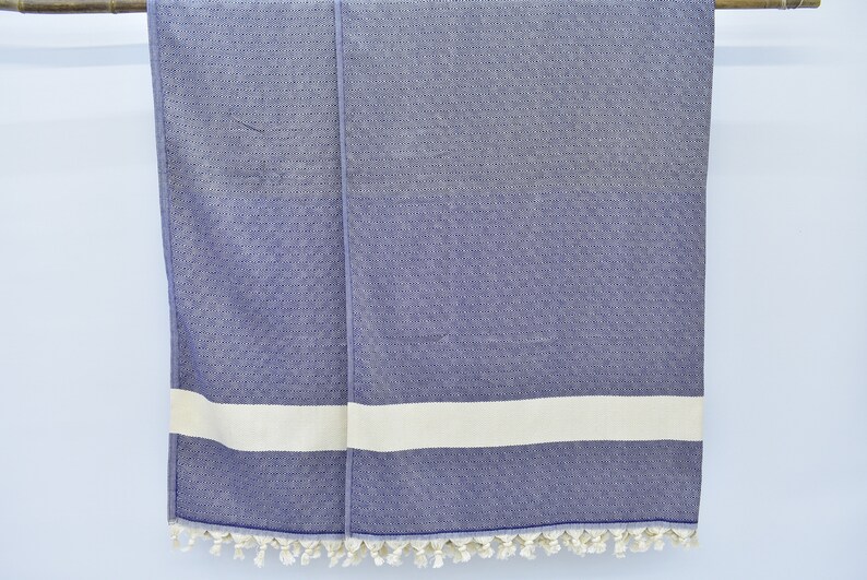 May include: A blue and white striped towel with fringe trim. The towel is hanging on a wooden rod.