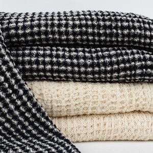 May include: A stack of four waffle weave towels in black and white and natural colors. The towels are folded and have a textured waffle weave pattern.