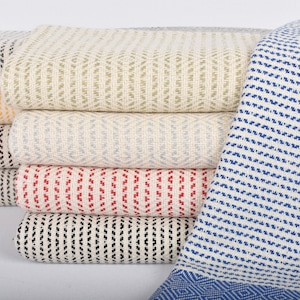 May include: A stack of woven cotton towels in various colors and patterns, including black, white, red, blue, and yellow. The towels are folded and arranged in a neat pile.