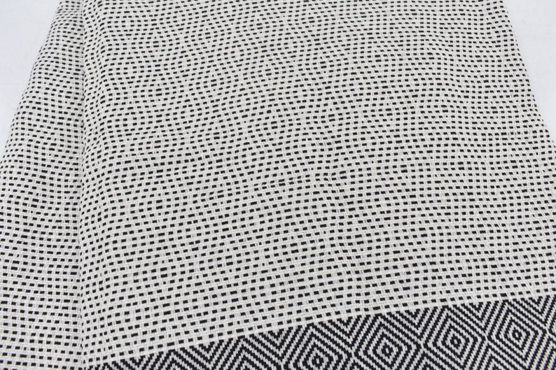 May include: A white and black patterned fabric with a geometric design. The fabric has a woven texture and a subtle sheen.