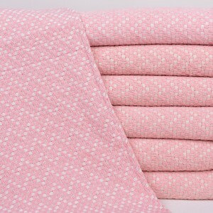 Può includere: Una pila di coperte di cotone tessute rosa e bianche. Le coperte sono piegate e impilate l'una sull'altra. Le coperte sono morbide e soffici.