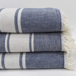Op de afbeelding: Een stapel van drie blauw-wit gestreepte handdoeken met franjes. De handdoeken zijn gevouwen en gestapeld op een wit oppervlak.