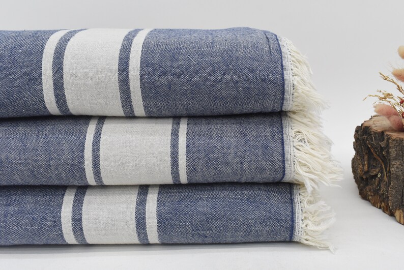 Op de afbeelding: Een stapel van drie blauw-wit gestreepte handdoeken met franjes. De handdoeken zijn gevouwen en gestapeld op een wit oppervlak.