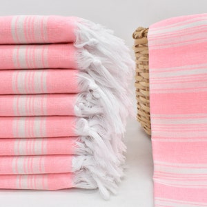 May include: A stack of pink and white striped towels with white fringe. The towels are folded and stacked on a white surface.