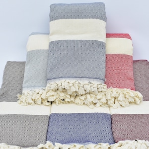 May include: A set of six Turkish towels in various colors, including gray, blue, and red. The towels are made of cotton and have a fringed edge. They are stacked on top of each other, with the top towel folded in half.